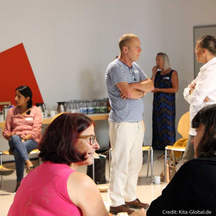 Teilnehmende des Workshops stehen verteilt im Raum in Zweiergruppen herum und unterhalten sich. 